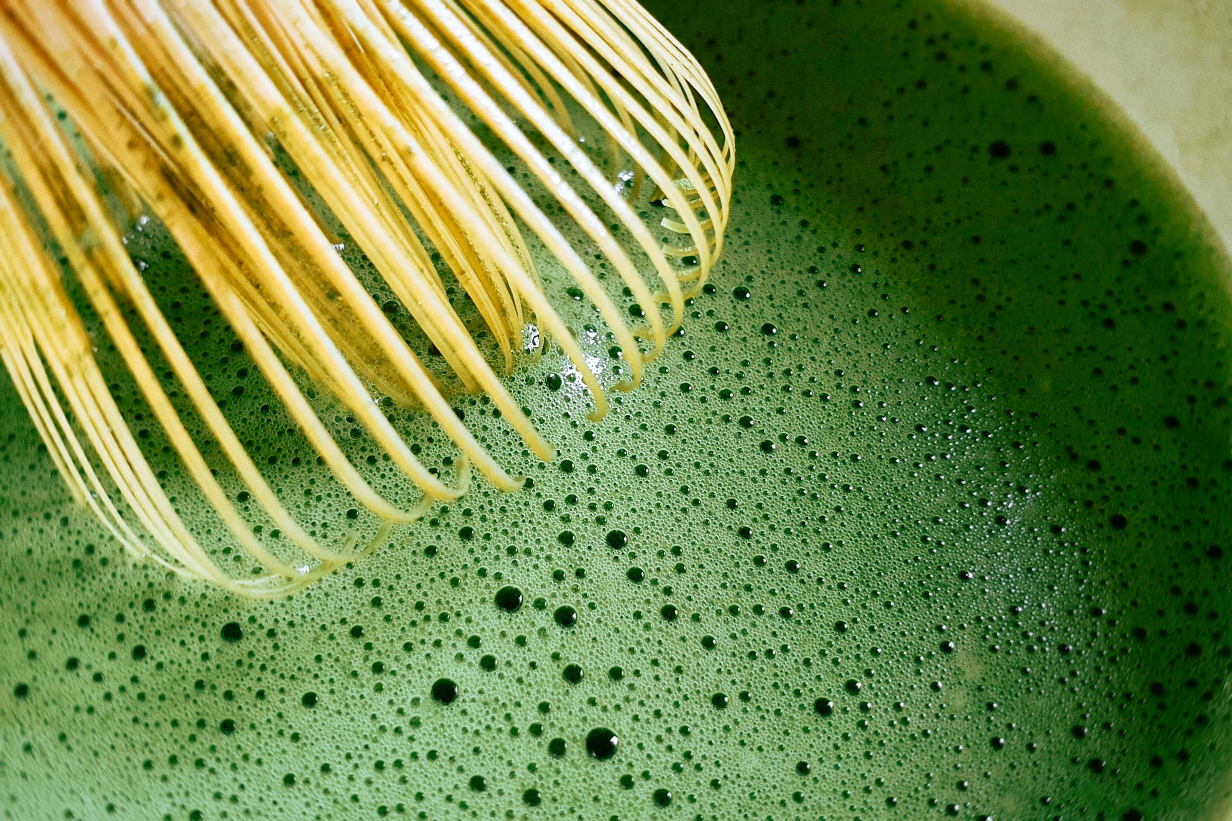 Bamboo whisk raising a fine green foam on freshly whisked matcha